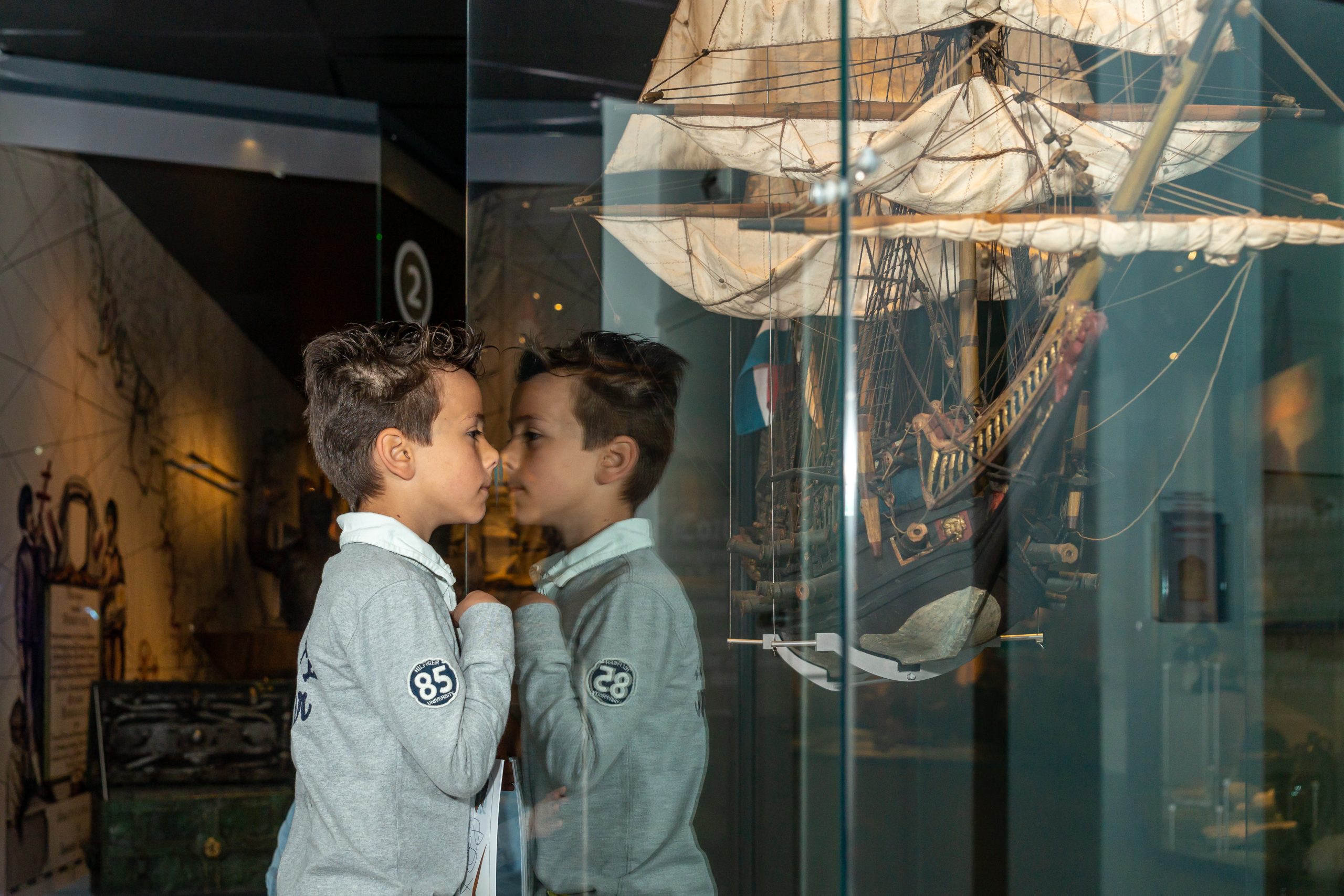 jongetje kijkt naar scheepsmodel in vitrine