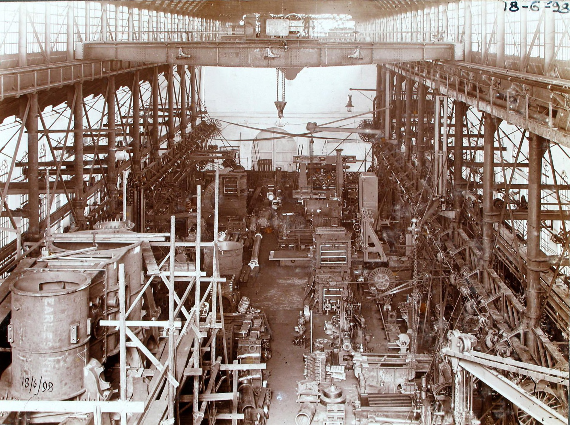 Een oude sepia kleurige foto die een inkijkje geeft in de ketelmakerij van De Schelde. De fotograaf kijkt van boven neer op veel verschillende industriële machines, ook zie je verschillende staal installaties, katrollen, lampen en ketels. In de hoek is de datum genoteerd: 18-6-1898.