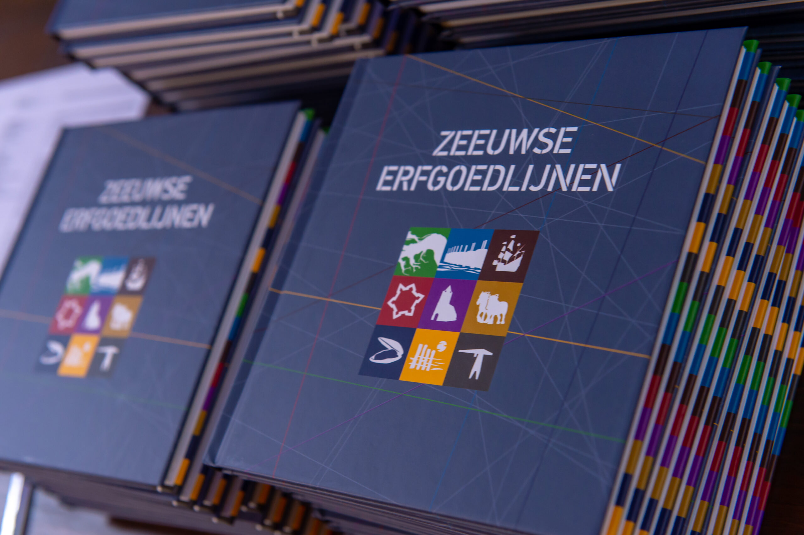Twee stapels boekjes met daarop de tekst 'Zeeuwse erfgoedlijnen' met daaronder de negen icoontjes van de erfgoedlijnen
